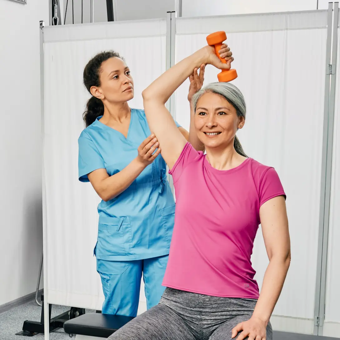 Work injury rehab: Lifting weights during FCE at rehabilitation clinic. Nurse assists. Mobility recovery, pain relief.